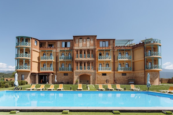 A multi-story hotel with a swimming pool, multiple balconies, and a central courtyard. - Burki Castle & Cellar (Kvareli)