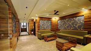 A modern lobby with a wooden accent wall, a green sofa, a glass coffee table, and a ceiling fan. - Hotel Sparkle Inn (Udaipur)