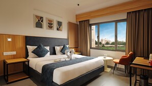 A modern hotel room with a large bed, a desk, and a view of the city. - Hotel Sparkle Inn (Udaipur)
