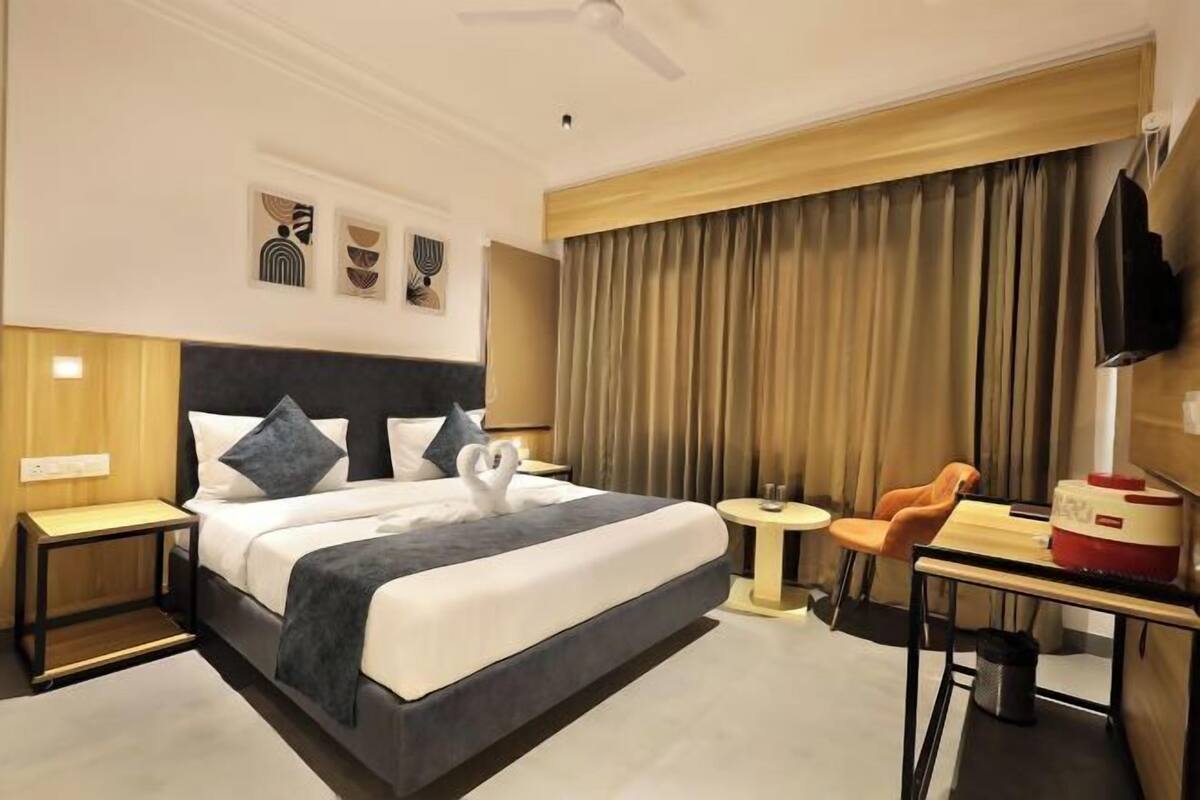 Habitación de hotel con cama, escritorio, silla, televisor y ventilador de techo.