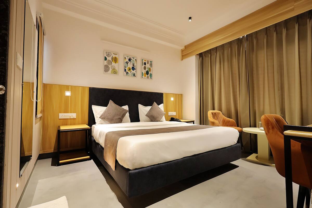 Una habitación de hotel moderna con una cama grande, dos mesitas de noche, una pequeña mesa redonda y dos sillas.