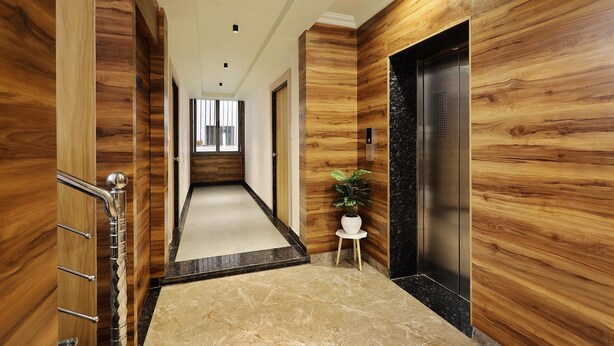 A modern hallway with wooden paneling, a marble floor, a small white table with a plant, and an elevator. - Hotel Sparkle Inn (Udaipur)
