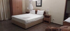 Une chambre d’hôtel avec un lit simple, une table de chevet, une commode et une armoire.
