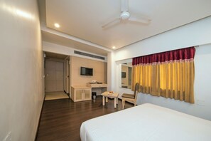 Una habitación de hotel con cama, escritorio, silla, televisión y ventana con cortinas.