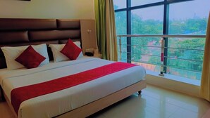 A hotel room with a large bed, a headboard, and a view of greenery through the window.