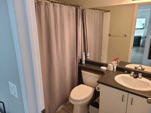 Een badkamer met douchegordijn, toilet, wastafel en spiegel.