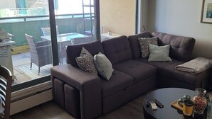 Un salon avec une grande fenêtre, un canapé, une table basse et une vue sur le balcon extérieur.