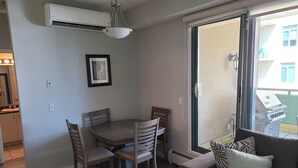 Un coin repas comprenant une table et des chaises, un luminaire au plafond et une porte-fenêtre coulissante donnant sur un espace extérieur équipé d’un barbecue.
