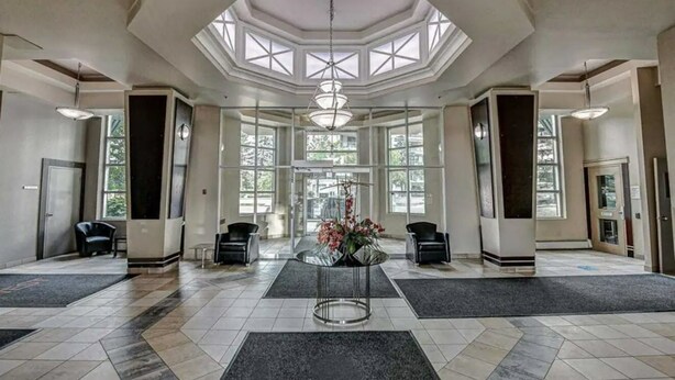 Un hall d’entrée spacieux, doté d’un haut plafond, de grandes fenêtres et d’une table ronde centrale agrémentée d’un arrangement floral.