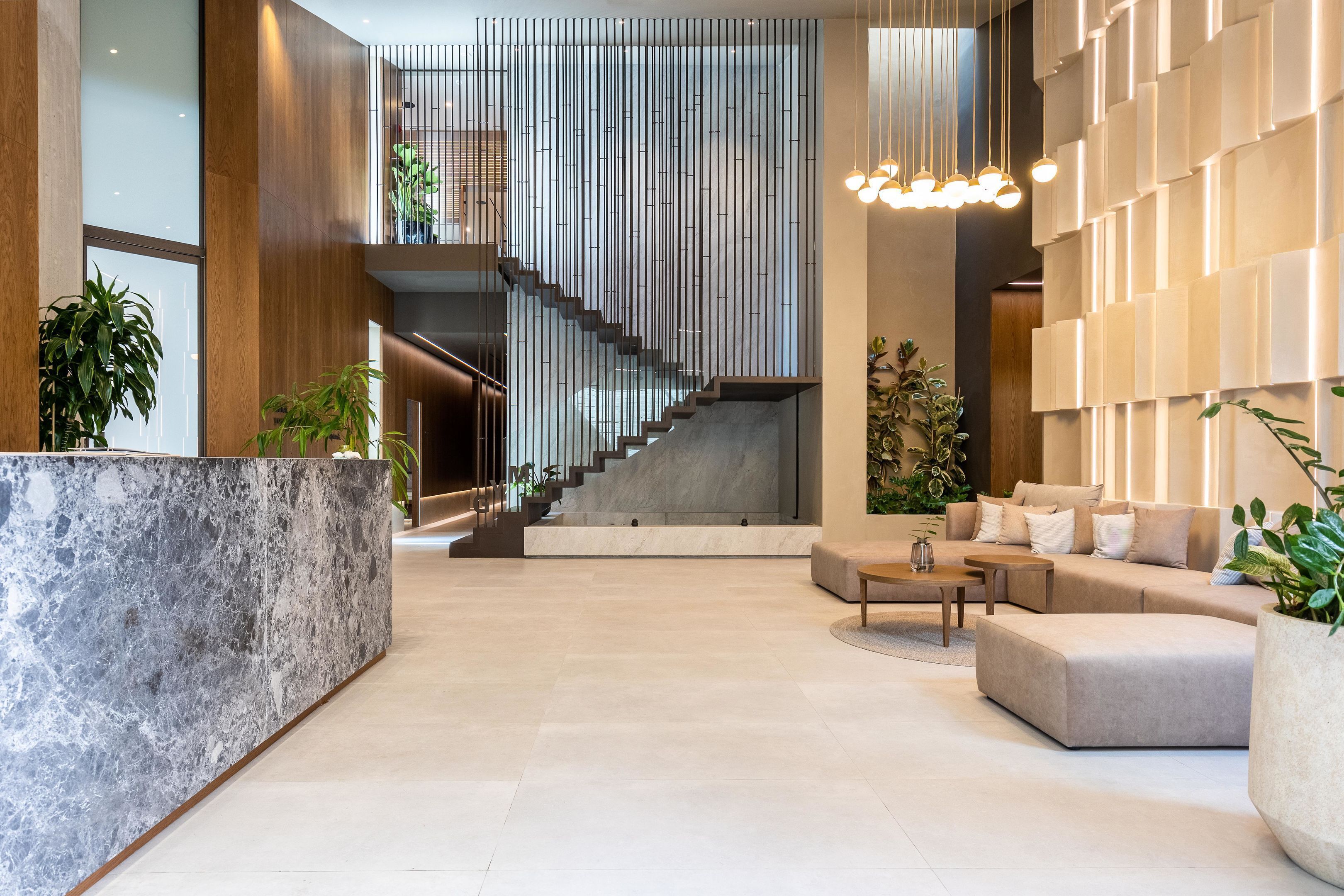 A modern lobby with a marble reception desk, a staircase, and a seating area with a sofa and coffee table.