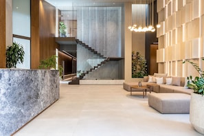 Un hall d’entrée moderne avec un comptoir de réception en marbre, un escalier et un espace détente comprenant un canapé et une table basse.
