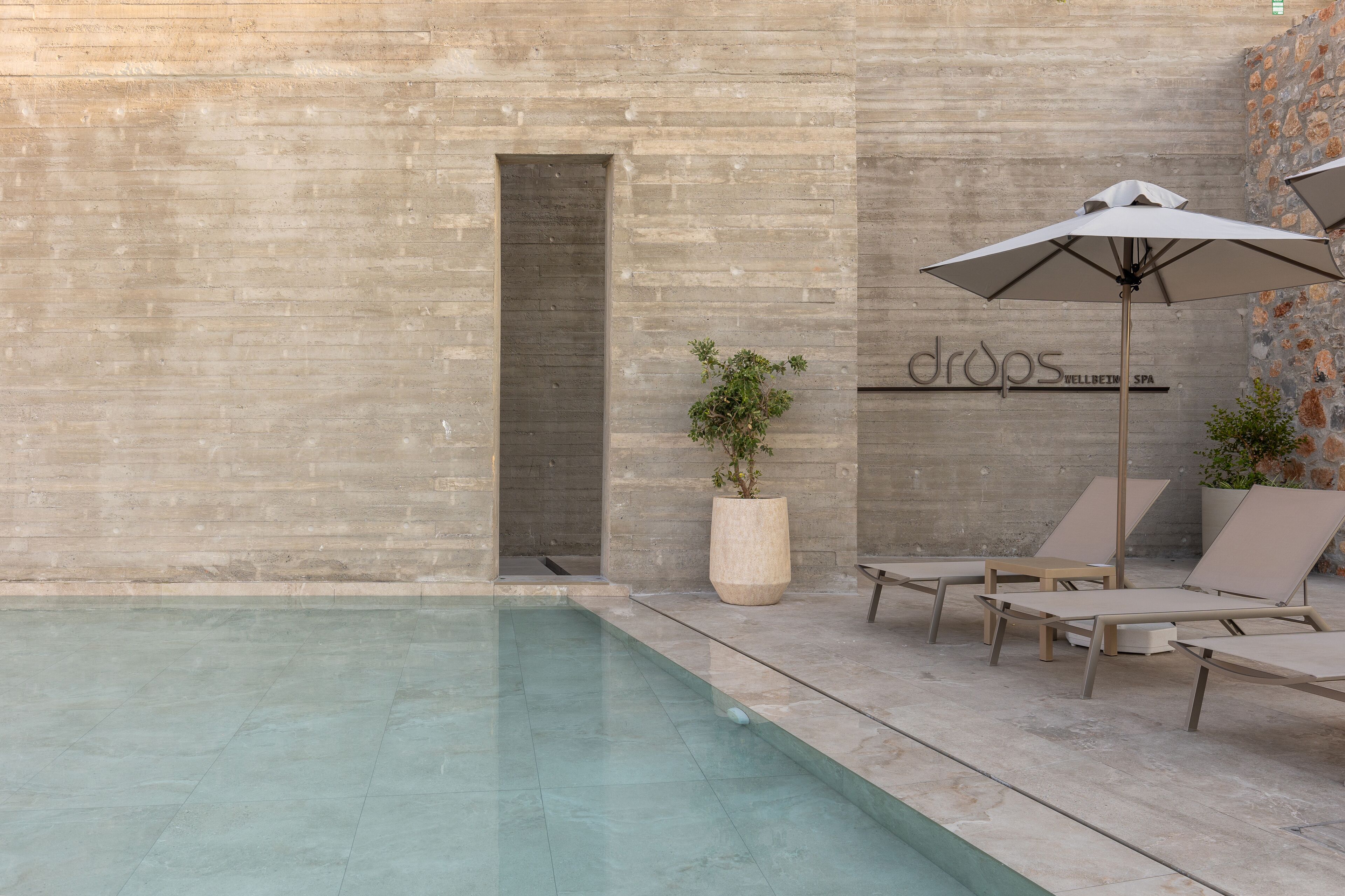 Zona de piscina con sillones de descanso y sombrillas, una planta en maceta y un letrero de spa.