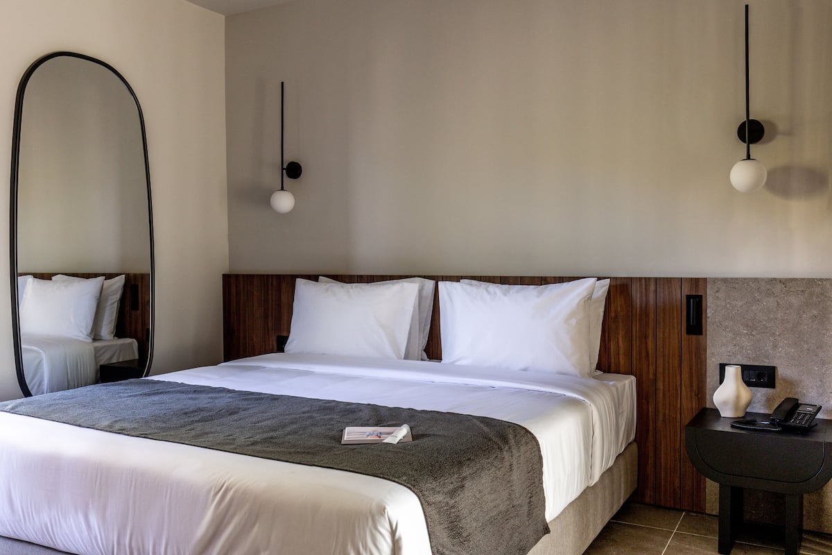 A hotel room with a large bed, a bedside table with a lamp, and a wall-mounted phone.