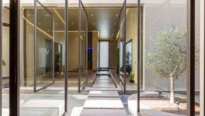 Une entrée moderne avec des portes en verre, un chemin central et un petit arbre.