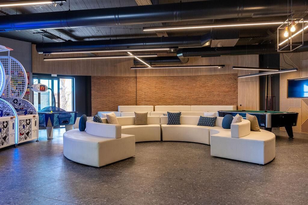 Un'area relax moderna con un divano bianco curvo, un tavolo da biliardo e un tavolo da calcio.