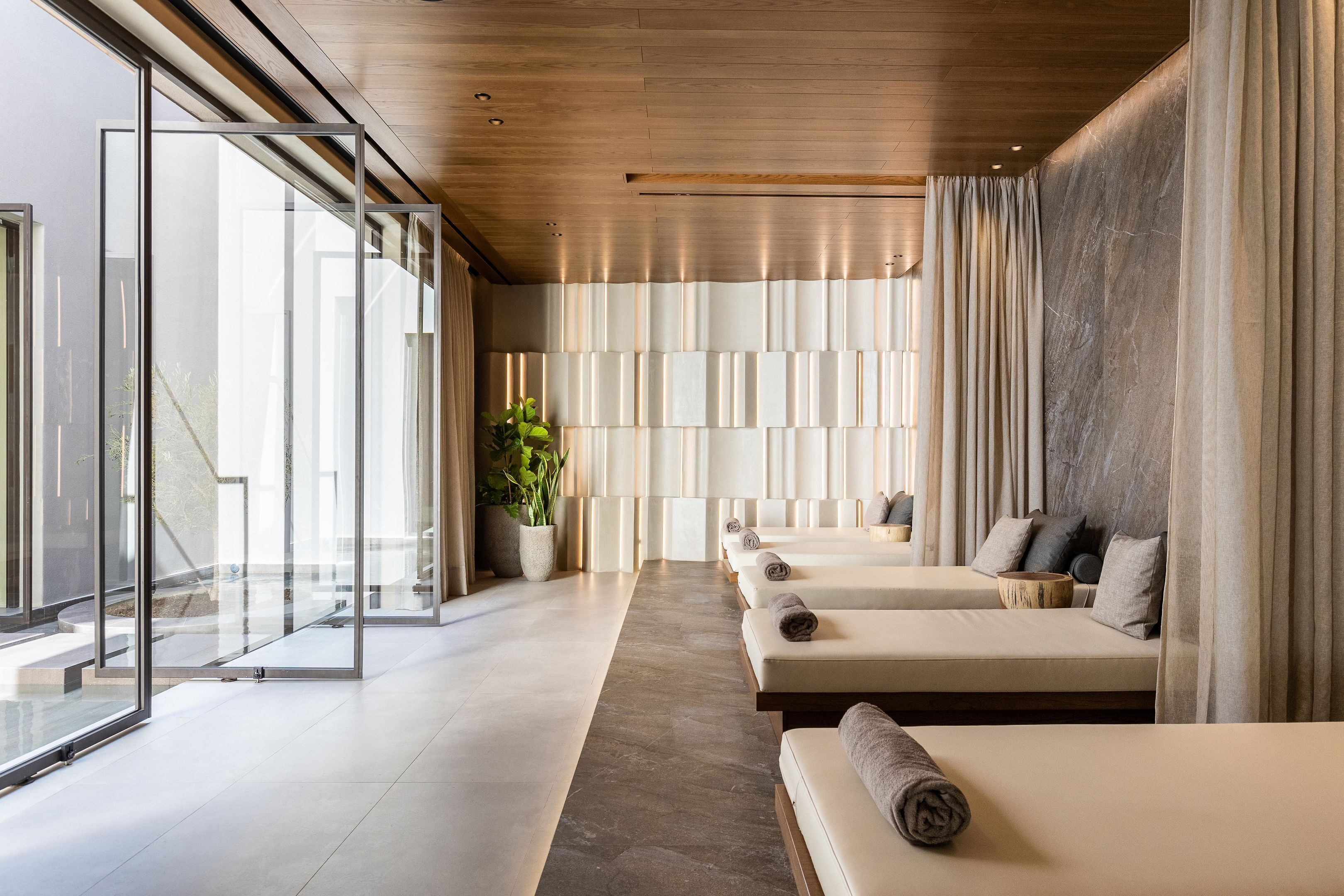 Un spa moderno con paredes de vidrio, techo de madera y una fila de camillas de masaje.