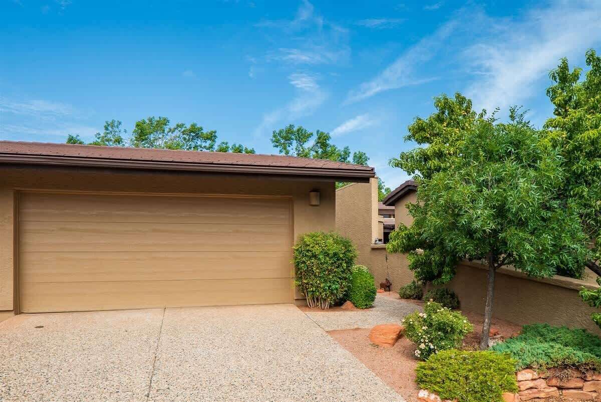 A residential garage with a brown door, surrounded by landscaped garden beds and a variety of shrubs.