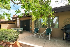 A patio with two green chairs, a table, and a barbecue grill.