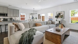 A modern living room with a sectional sofa, a wooden coffee table, and a kitchen area with white cabinets and a microwave.