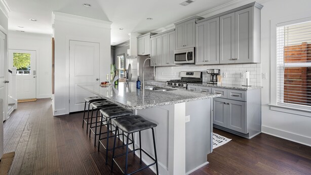 A modern kitchen with grey cabinets, a large island with bar stools, and a view of the outdoors.