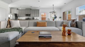 A modern living room with a grey sofa, a wooden coffee table, and a kitchen in the background.