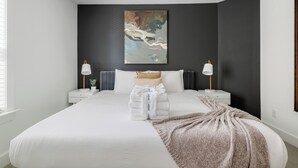 A modern hotel room with a large bed, dark accent walls, and a painting above the bed.