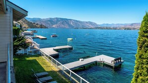 A lakeside property with a dock, boats, and a mountain backdrop. - 3Bed, 2.5Bath Waterfront Home with Boat Lift! (Chelan)