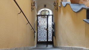 A staircase leading to a door with a decorative metal gate, flanked by potted plants and a small shelf. - Residenza Amalphia (Amalfi)