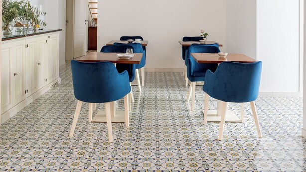 A dining area with a patterned floor, blue chairs, and a white ceiling with decorative elements. - Residenza Amalphia (Amalfi)