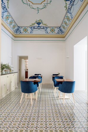 Un espace repas doté d’un sol à motifs, de chaises bleues et d’un plafond blanc agrémenté d’éléments décoratifs.