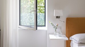 A room with a bed, a small bedside table with a lamp, a window with curtains, and patterned floor tiles. - Residenza Amalphia (Amalfi)
