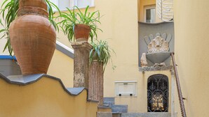 A staircase with potted plants on the landing, a white door, and a decorative metal gate at the bottom. - Residenza Amalphia (Amalfi)