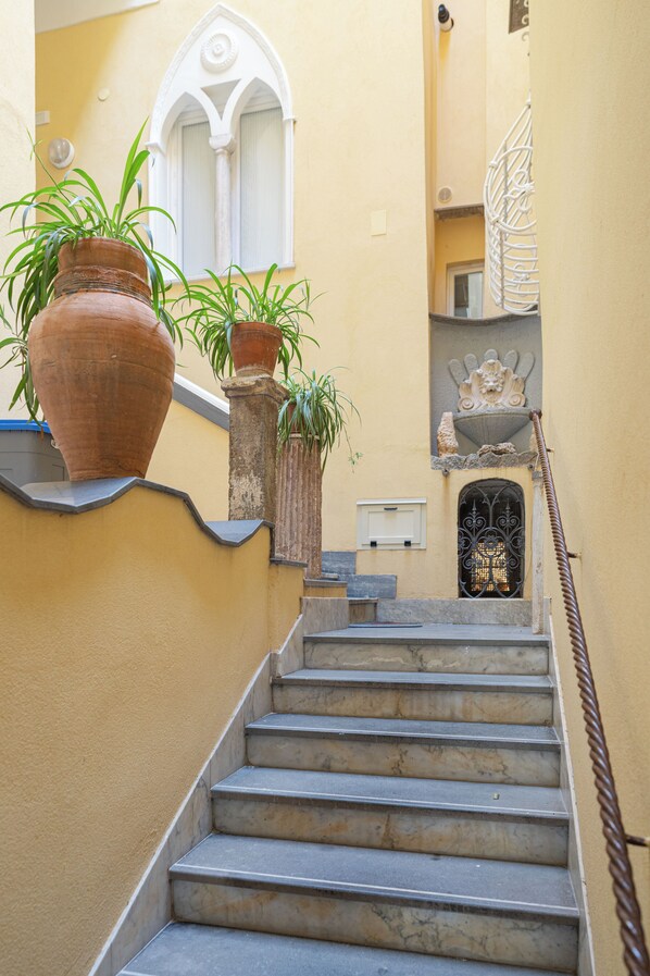 A staircase with potted plants on the landing, a white door, and a decorative metal gate at the bottom.