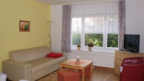 A living room with a sofa, a coffee table, a TV, and a window with curtains.