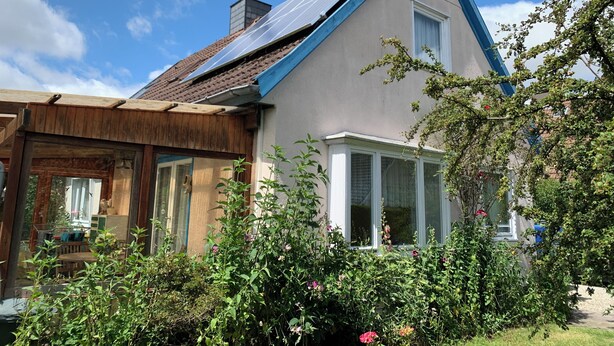 A house with a sloped roof, solar panels, and a garden with various plants and flowers.