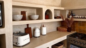 A kitchen with a modern design, featuring a toaster, kettle, and a stove. Shelves with bowls and a decorative item are also visible.