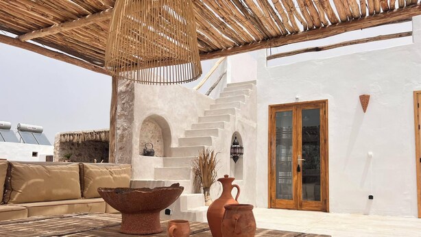 A rustic outdoor seating area with a wooden table, terracotta pots, and a woven ceiling.