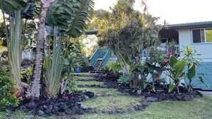A tropical garden with a variety of plants and a small building with a blue roof. - Seaside House, a Peaceful 2 Bedroom Retreat in walking distance to Kehena Beach (Pahoa)