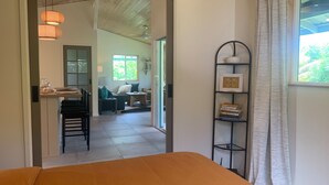 A hotel room with a wooden bed, a desk with a lamp, a bookshelf, and a view of the garden through the window. - Seaside House, a Peaceful 2 Bedroom Retreat in walking distance to Kehena Beach (Pahoa)