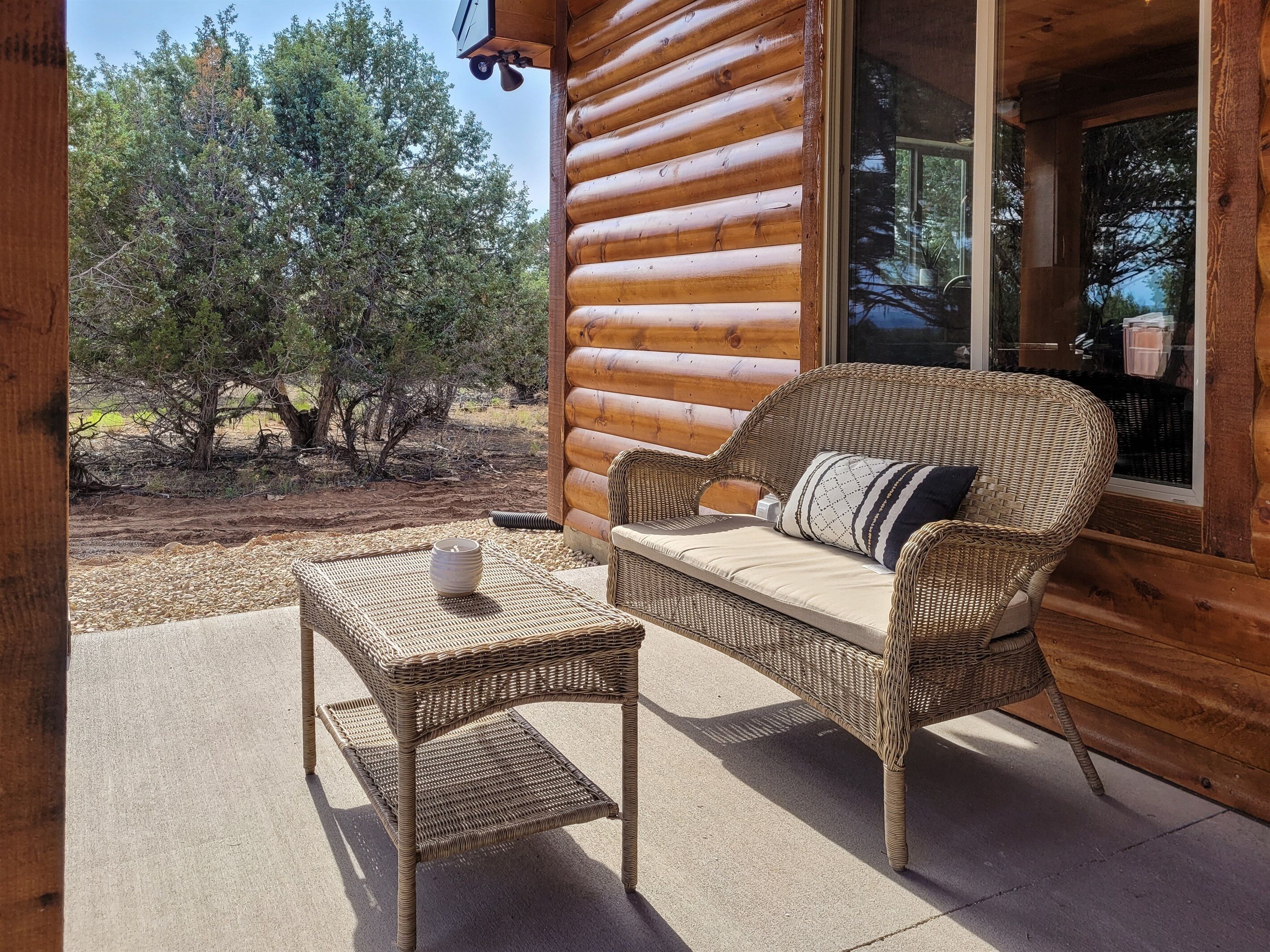 A log cabin with a wicker sofa and a small table on the porch.