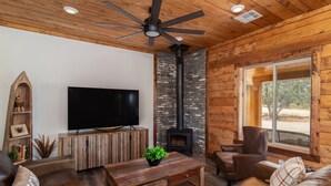 Una sala de estar acogedora con techo de madera, chimenea, muebles de cuero y un televisor grande.