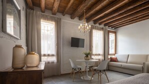 Une pièce chaleureuse avec un plafond en bois, une table à manger ronde entourée de chaises, un canapé et un téléviseur fixé au mur.