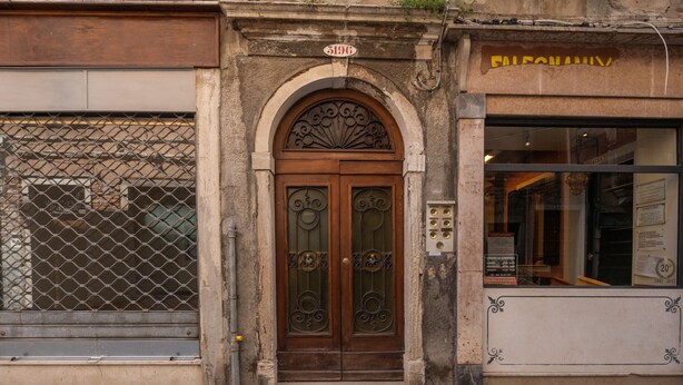 Un bâtiment doté d’une grande porte à double battant en bois, d’une enseigne au-dessus de la porte et d’une fenêtre ornée d’une grille métallique.