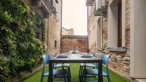 Une petite cour étroite avec une table dressée pour deux personnes, entourée de chaises bleues, et un mur de briques sur un des côtés.