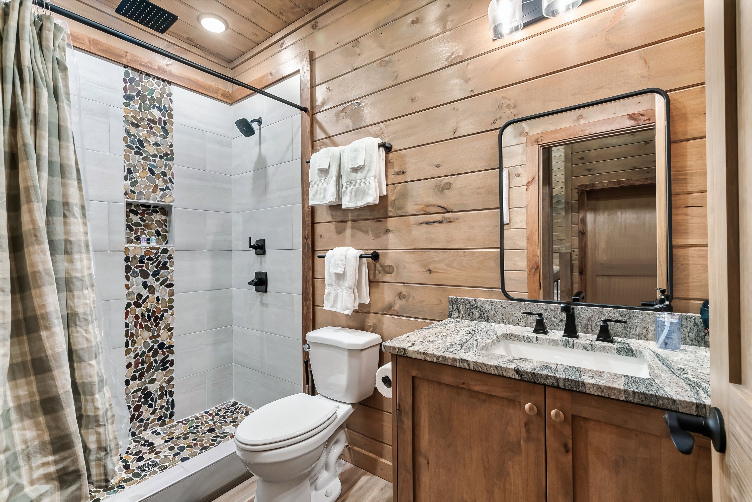 Ein Badezimmer mit Holzwandverkleidung, Dusche, Toilette und Waschtisch.
