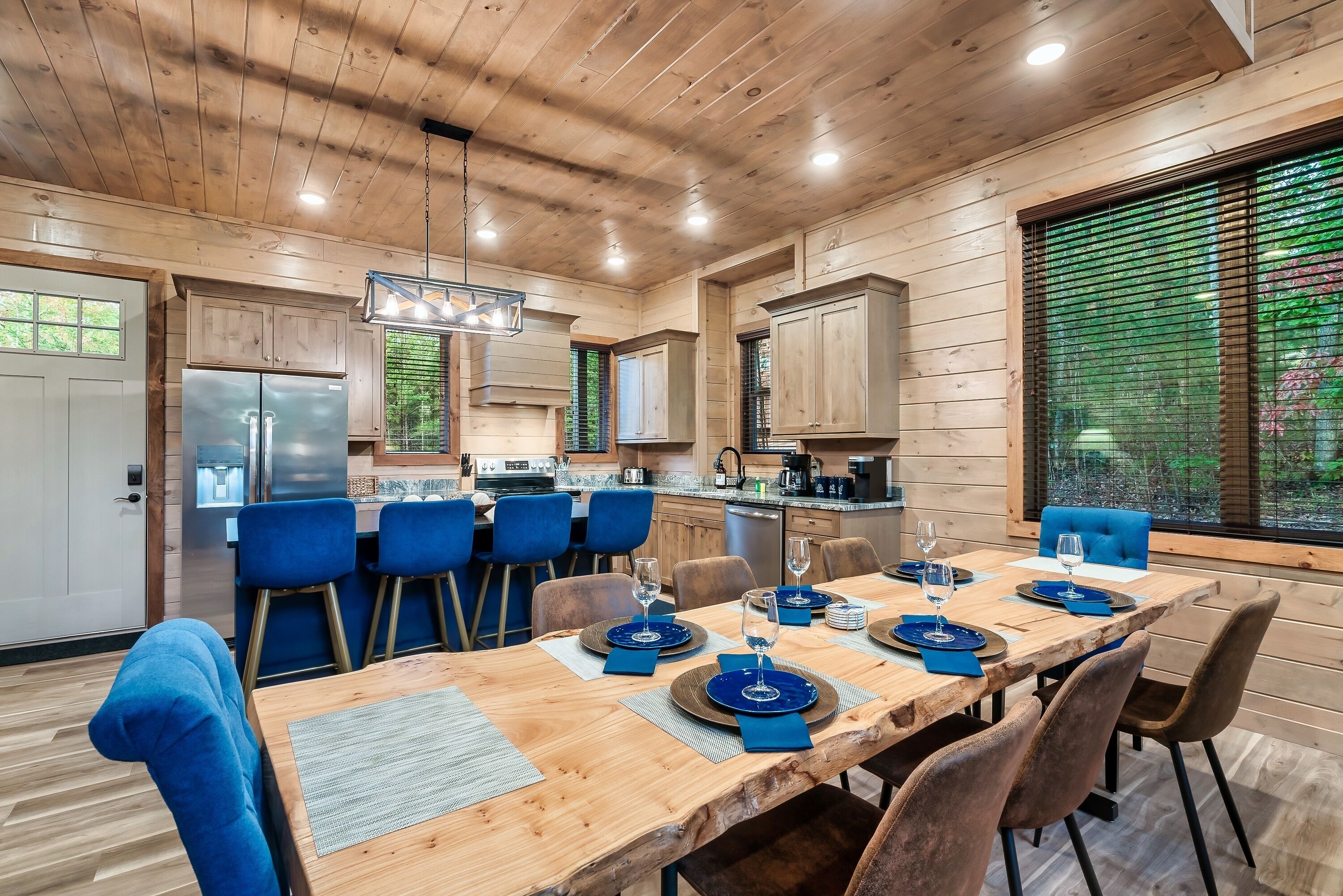 Une cuisine moderne avec des meubles en bois, un réfrigérateur en acier inoxydable et un coin repas avec des chaises bleues et une table en bois, le tout disposé pour accueillir quatre personnes.