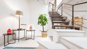 Un interior moderno con una escalera, una mesa redonda con una lámpara, una planta en maceta y un recipiente rojo.