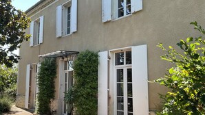A two-story building with white shutters, a covered entrance, and a small garden area with potted plants and a pathway. - Maison Dulcis (Saint-Maixant)