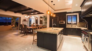 Una cocina moderna con armarios oscuros, una isla con encimera de granito y un comedor con mesa y sillas.