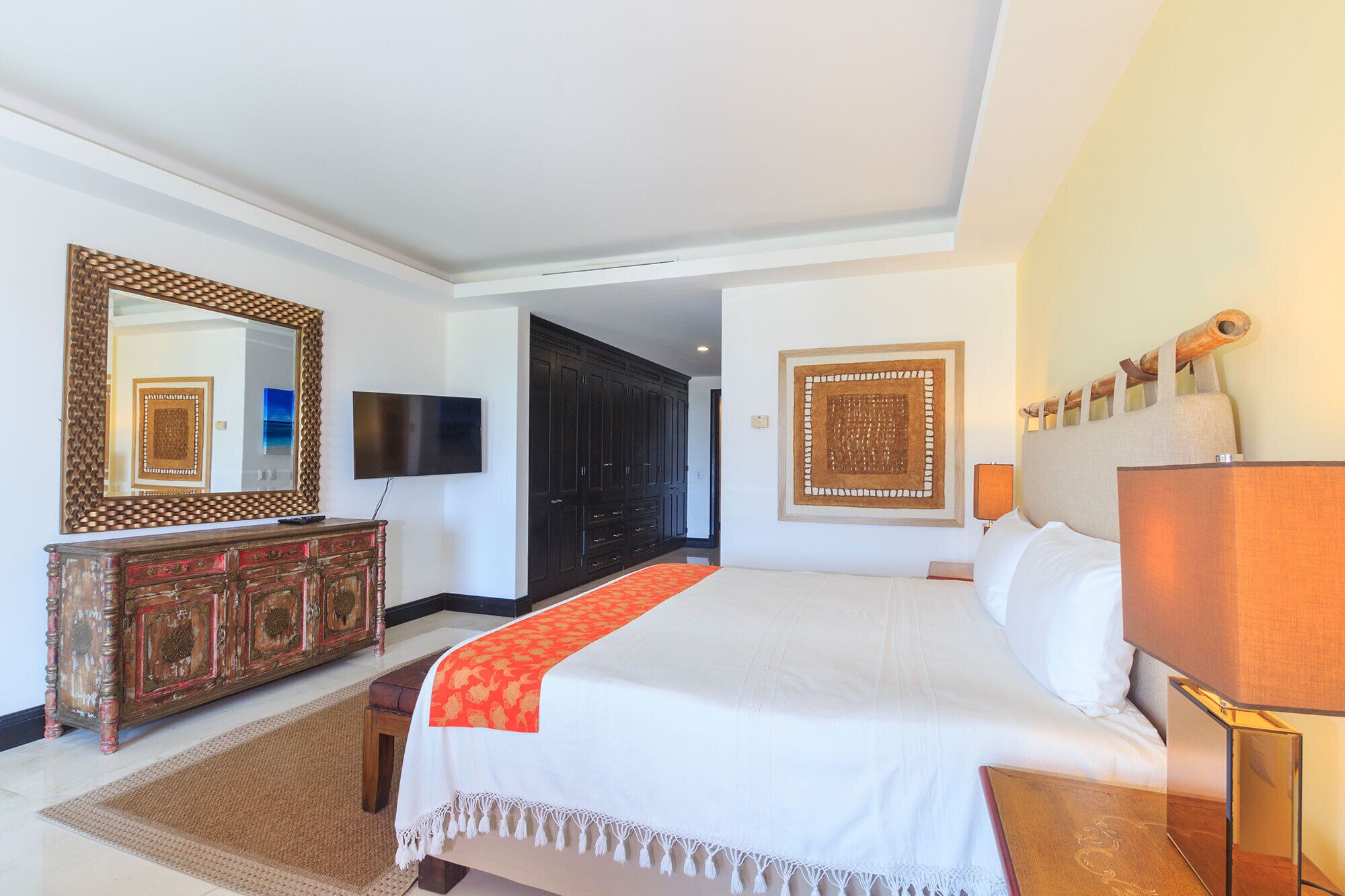 Une chambre d’hôtel avec un grand lit, une commode en bois, une télévision et un miroir décoratif.